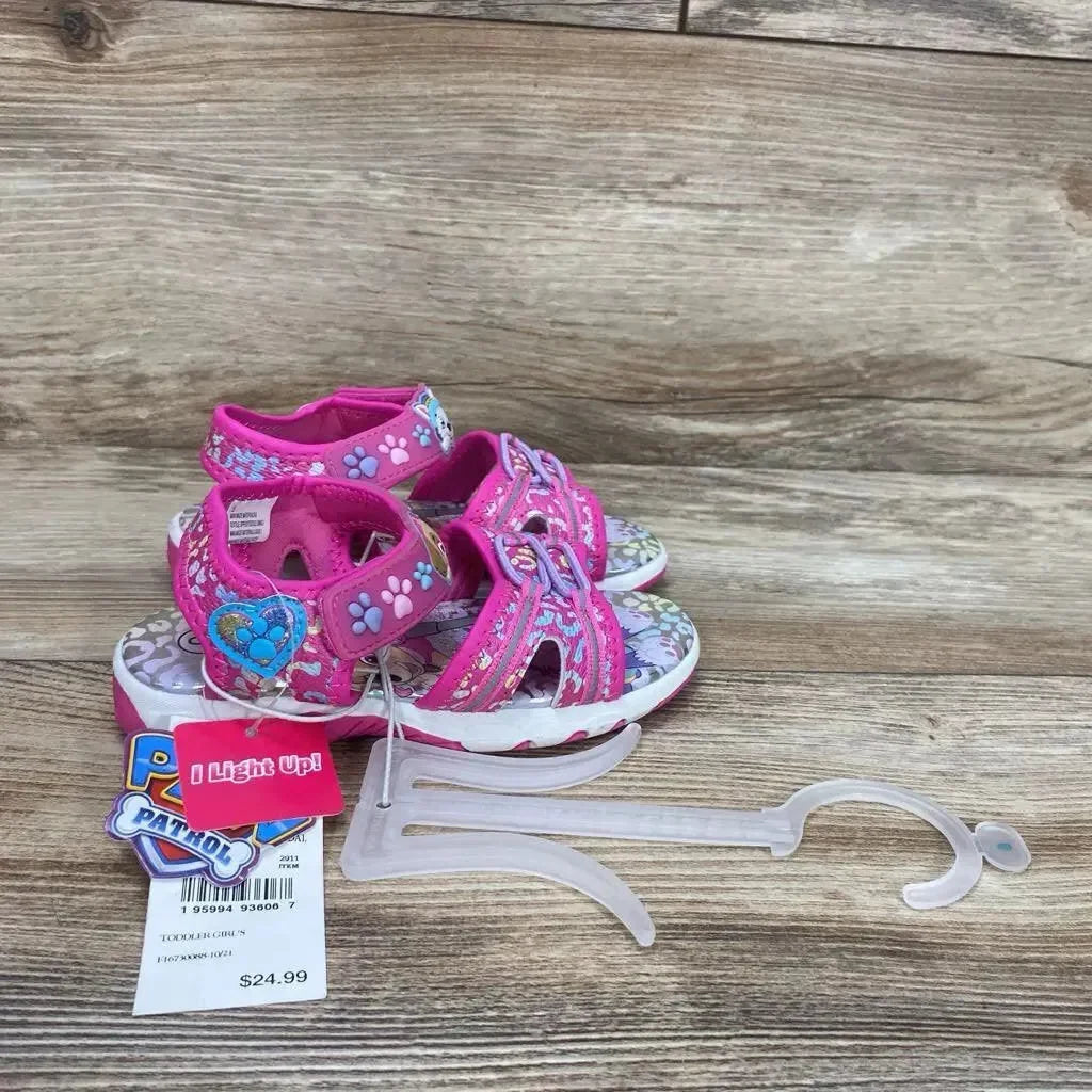 Side view of pink Paw Patrol ankle-strap sandals size 9C showcasing paw-print straps, heart badge, patterned footbed on wood