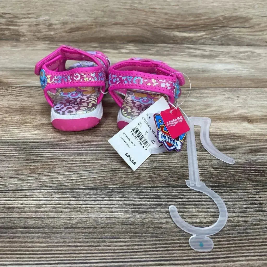 Back view of pink Paw Patrol kids ankle-strap sandals with glitter straps, velcro closure, and attached light-up tag on wood