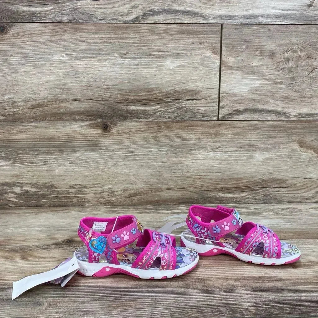 Side view of pink Paw Patrol ankle-strap toddler sandals showcasing paw-print straps and character-printed footbed on wood-plank background