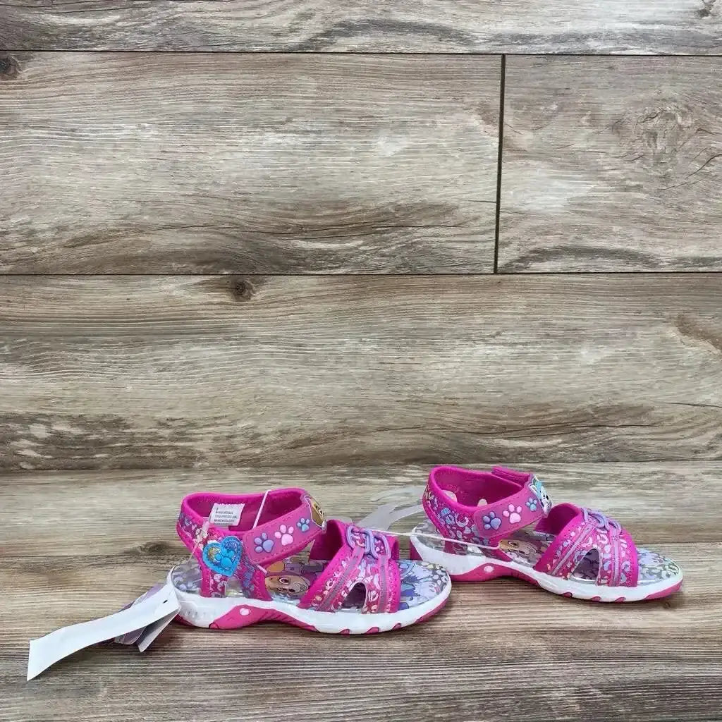 Side view of NWT Paw Patrol pink ankle strap sandals sz 9c showcasing character print footbed and hangtags on wood plank background