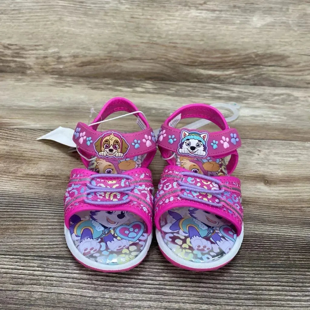 Front view of pink Paw Patrol toddler ankle-strap sandals (size 9C) showing character patches on straps and printed footbeds on wooden surface