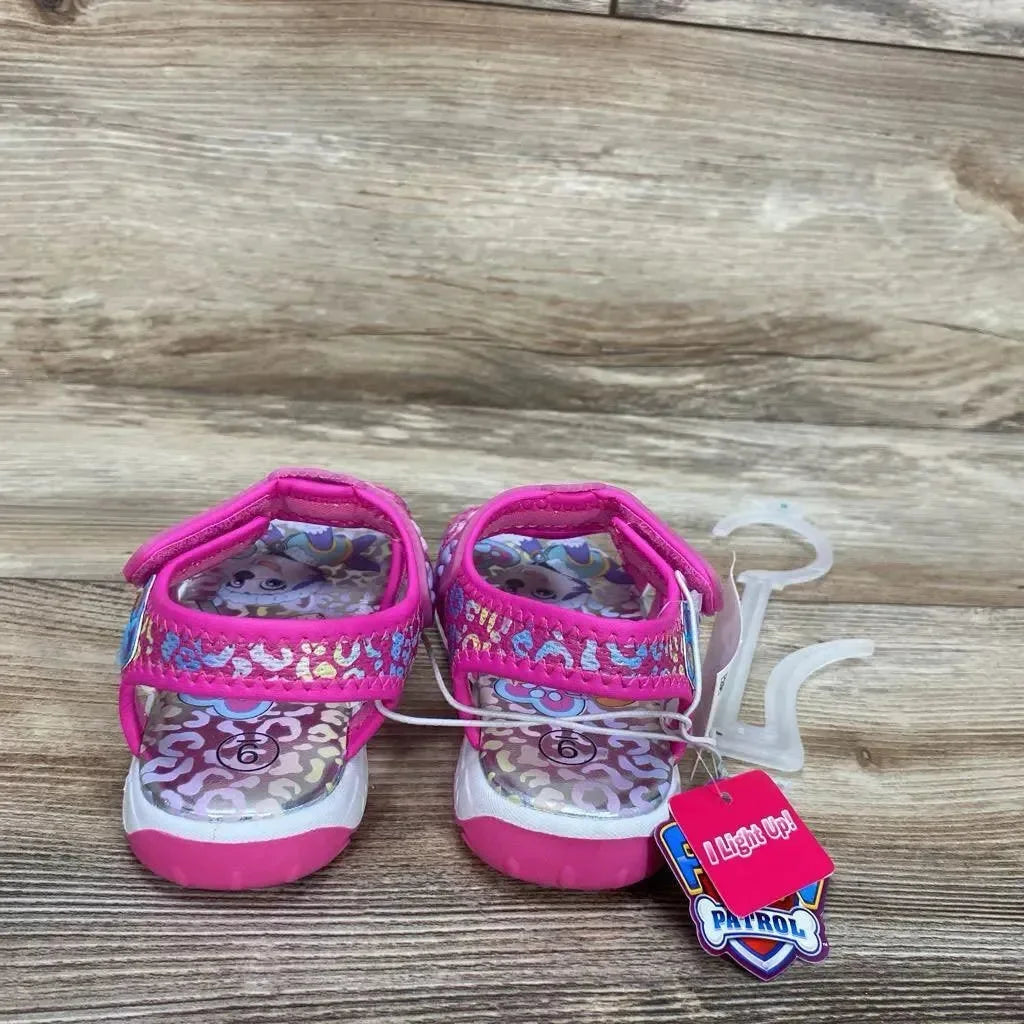 Front view of pink Paw Patrol toddler ankle-strap sandals showing patterned insoles and light-up tag on wooden floor