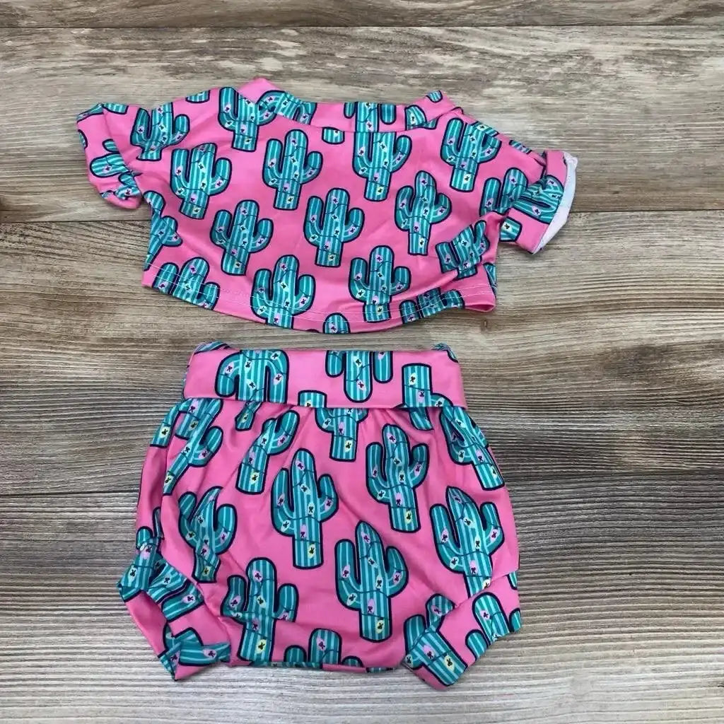 Flat lay of pink 2-piece baby shirt and bloomers with teal cactus print, elasticized waist and leg openings on wood background