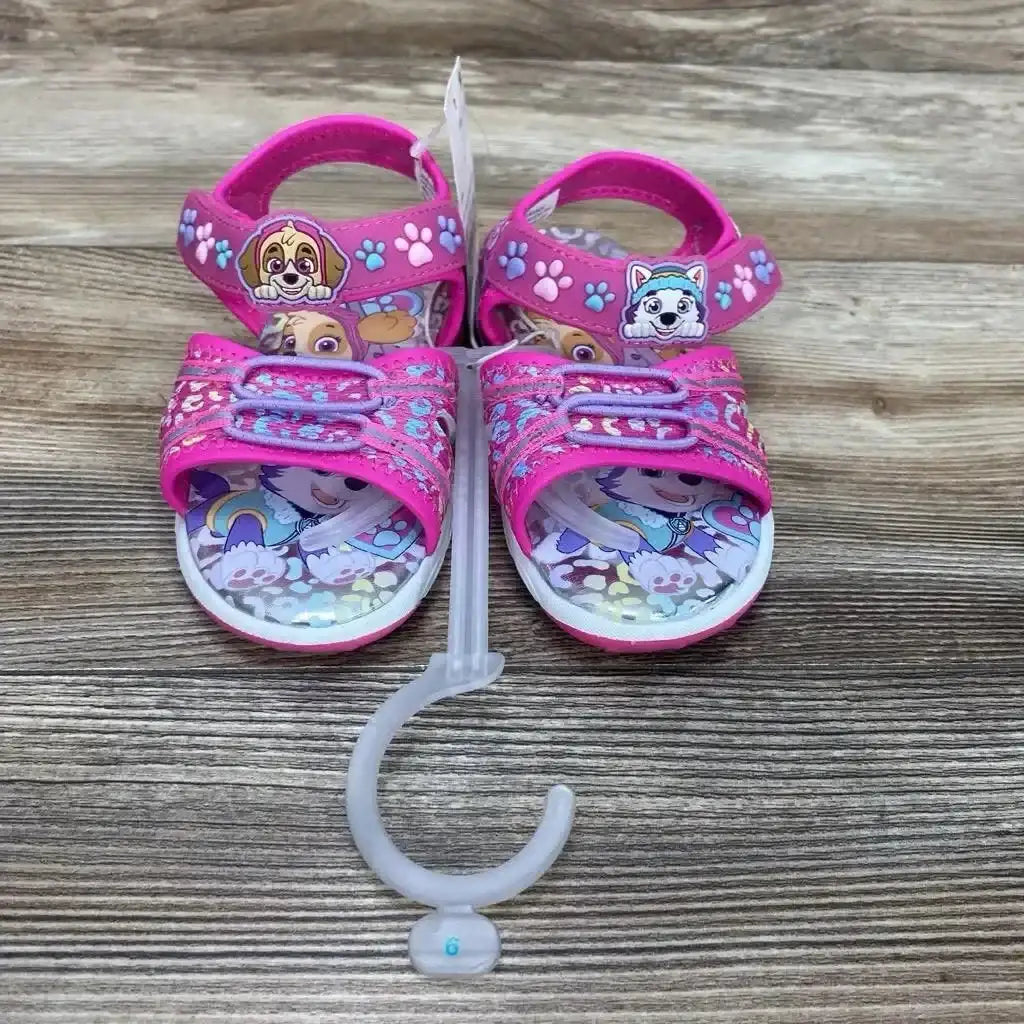 Front view of pink Paw Patrol sandals with character insoles, adjustable Velcro straps, and paw-print straps on wood