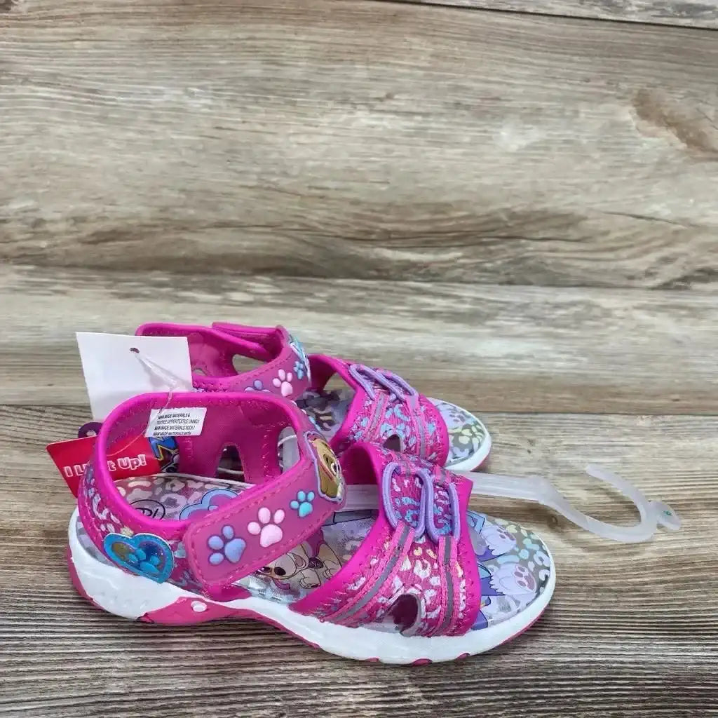 Top view of NEW Paw Patrol Adventure Ankle Strap Sandals sz 9c showcasing pink paw print straps and Skye graphic with retail tag on wood background