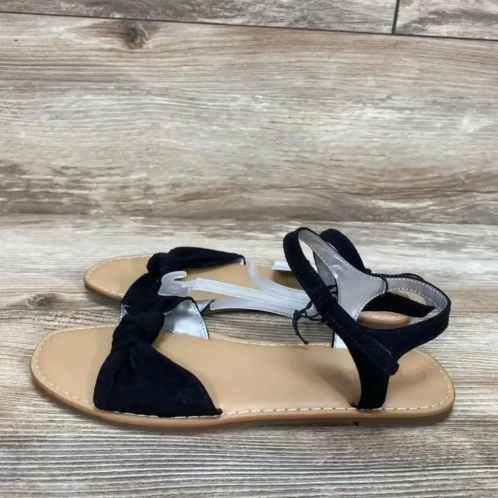 Side view of Cat and Jack Lydia toddler sandals (black, size 4Y) showcasing knotted front strap and ankle strap on wood plank background