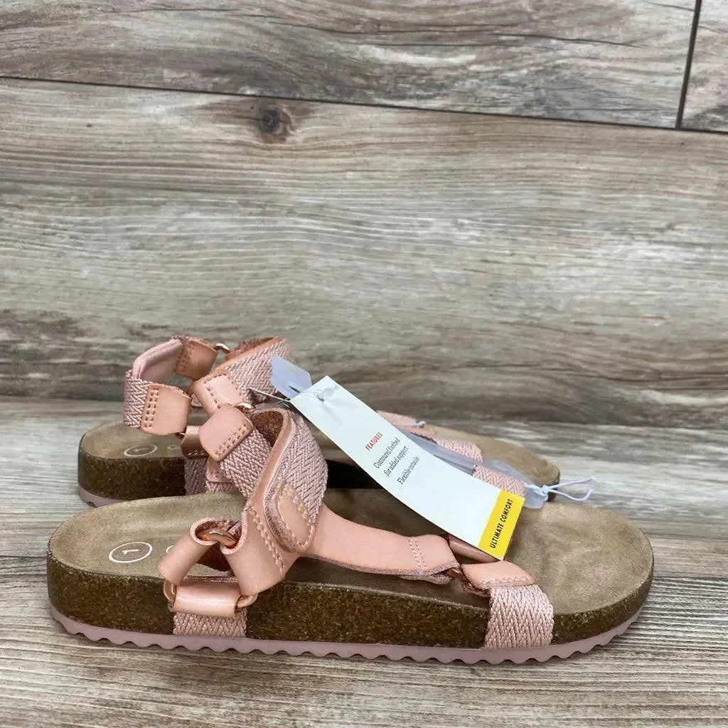 Side view of Cat & Jack Val toddler sandals in blush showing cork footbed, adjustable woven straps and hook-and-loop closures on a wood floor background