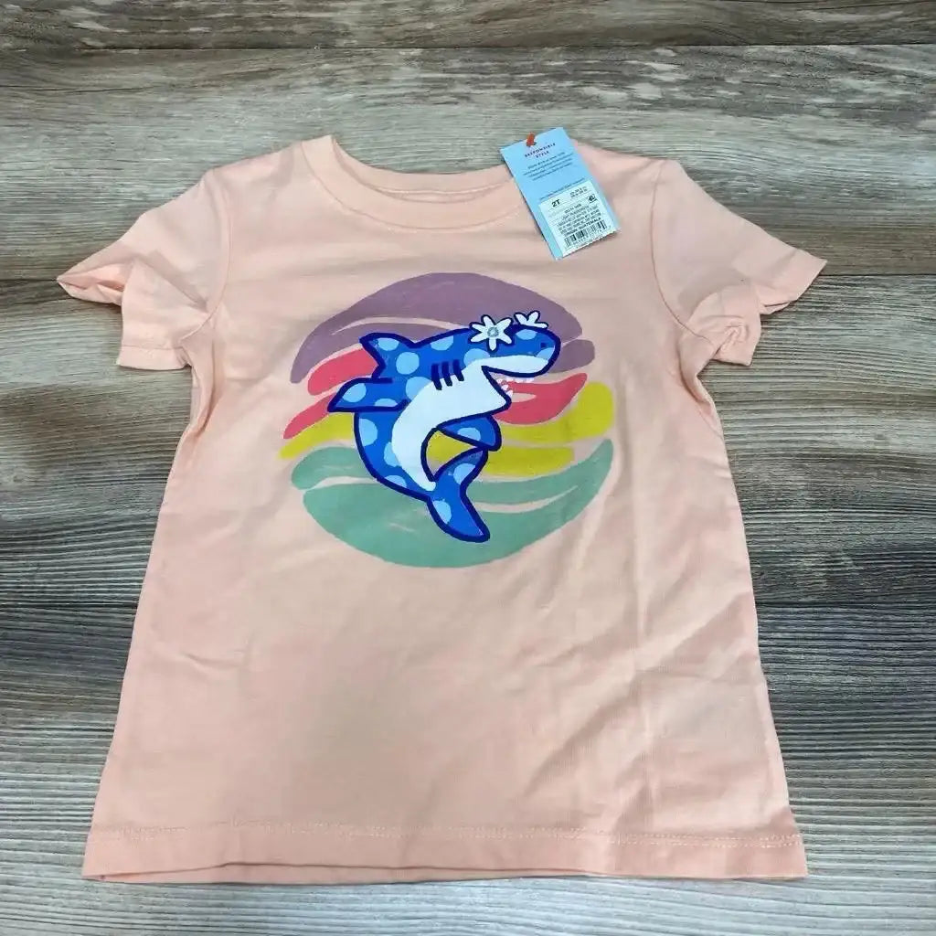 Front view of peach Cat & Jack 2T toddler tee with blue shark graphic and multicolor circle, tag at collar on wood background