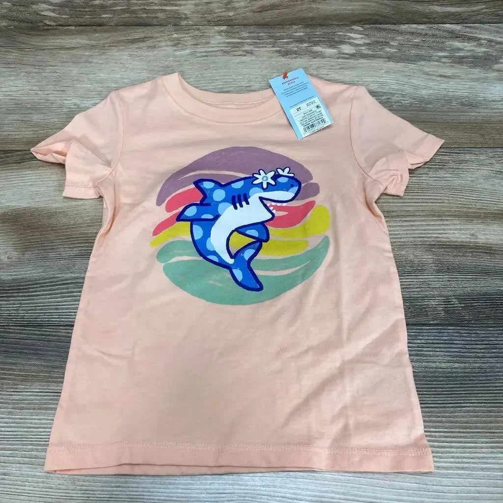 Front view of peach Cat & Jack 2T toddler tee with blue shark graphic and multicolor circle, tag at collar on wood background