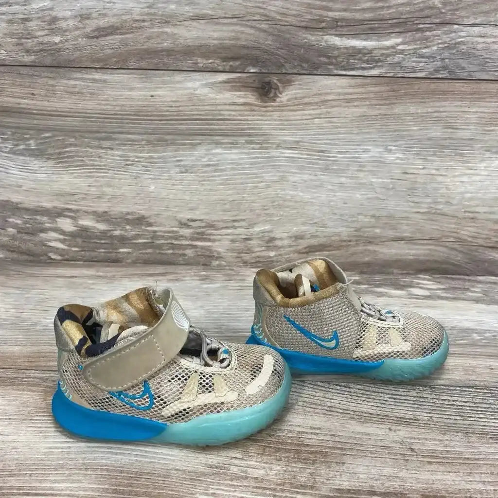 Side view of size 4C Nike Kyrie 7 sneakers, tan mesh with blue Swoosh, velcro strap and blue sole on wood background