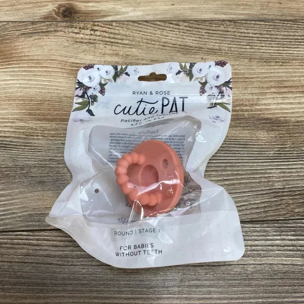 Top-down view of Ryan & Rose cutiePAT round pink pacifier with beaded teether in sealed packaging on wood background
