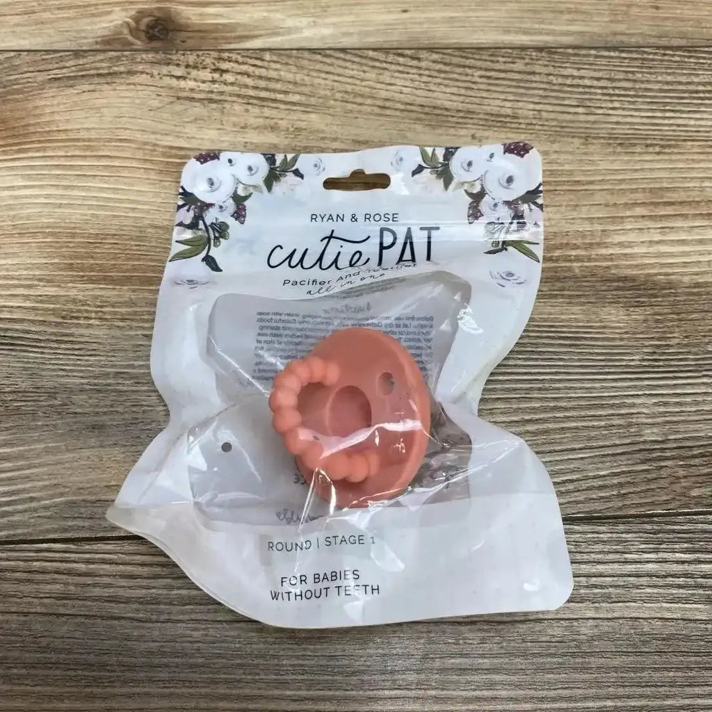 Top-down view of Ryan & Rose cutiePAT round pink pacifier with beaded teether in sealed packaging on wood background