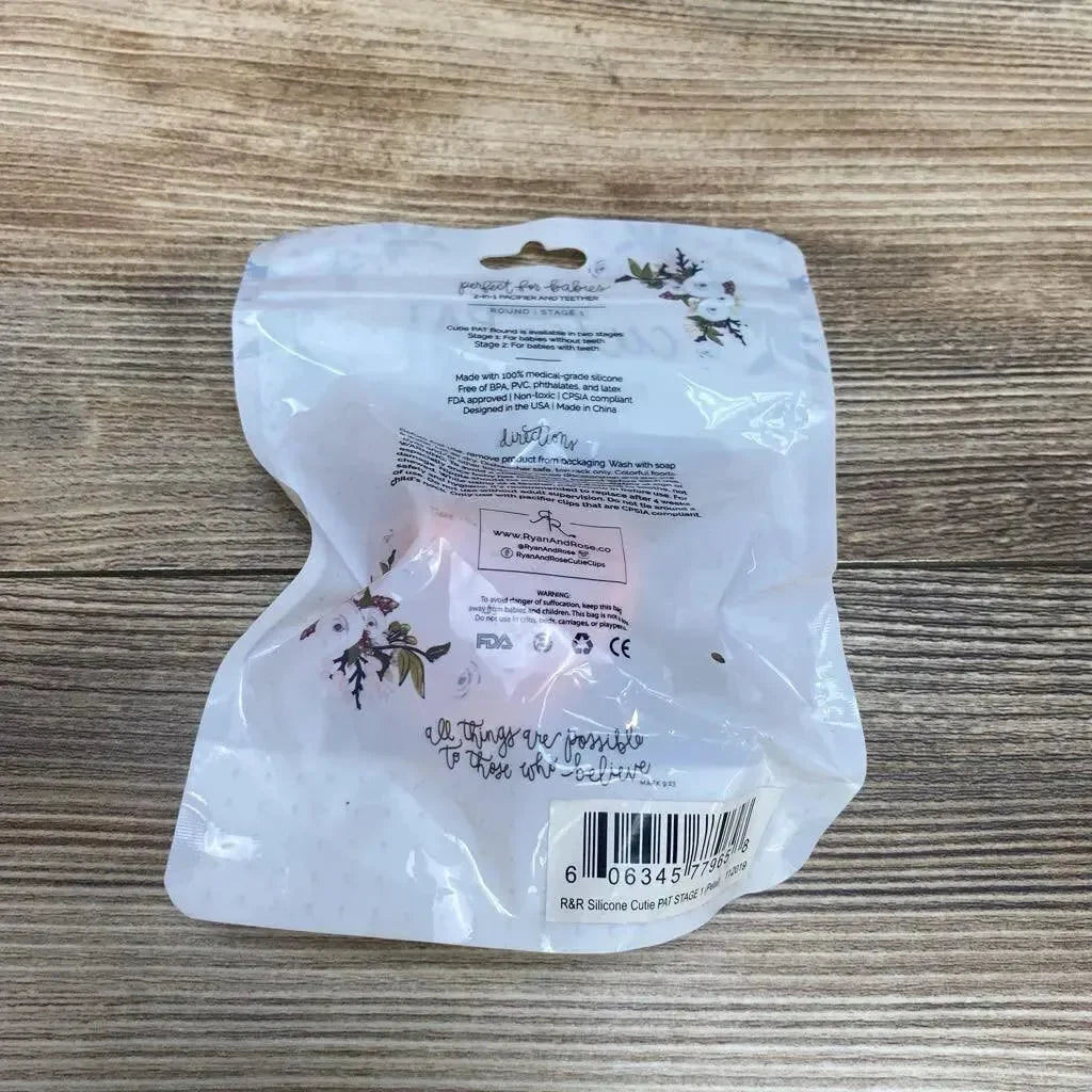 Rear view of Ryan and Rose Cutie PAT round pacifier and teether 0-6m in sealed floral pouch showing barcode on a wooden table