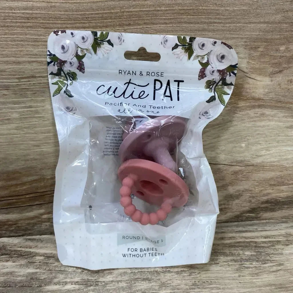Front view of Ryan & Rose Cutie PAT round pacifier and teether, pink silicone in clear retail pouch on wooden background