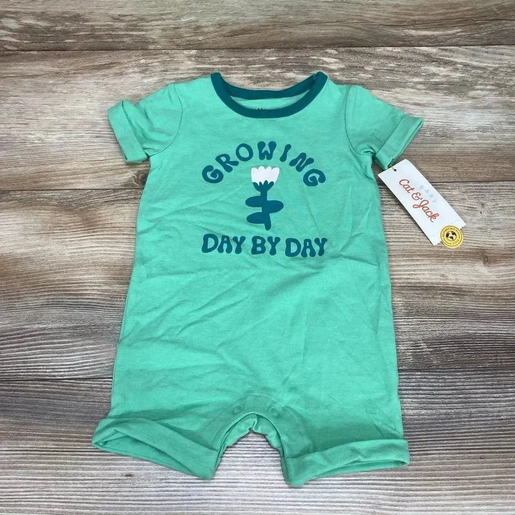 Flat-lay of green Cat & Jack romper saying Growing Day By Day with flower graphic, snap crotch and tag on wood background