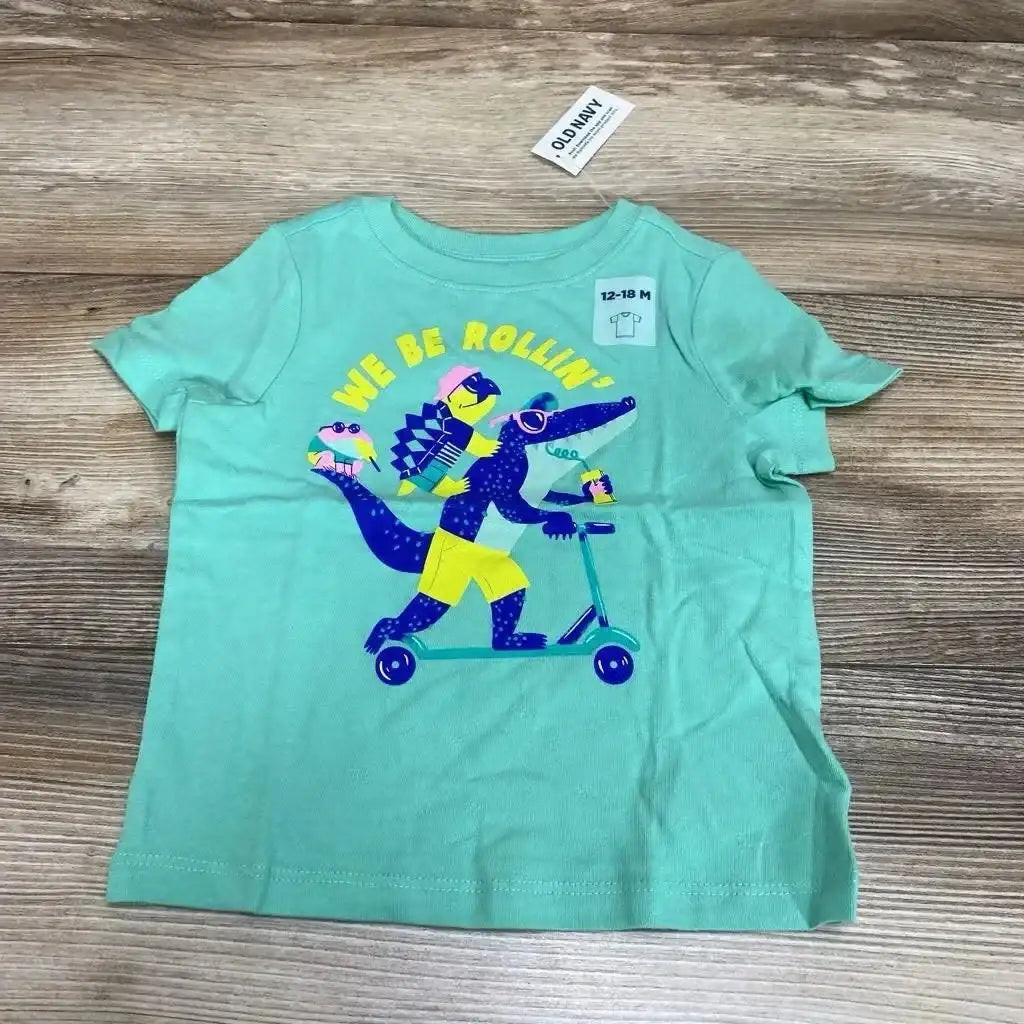 Flat lay of mint green toddler T-shirt with colorful alligator on scooter graphic and 12-18M size tag on wood background