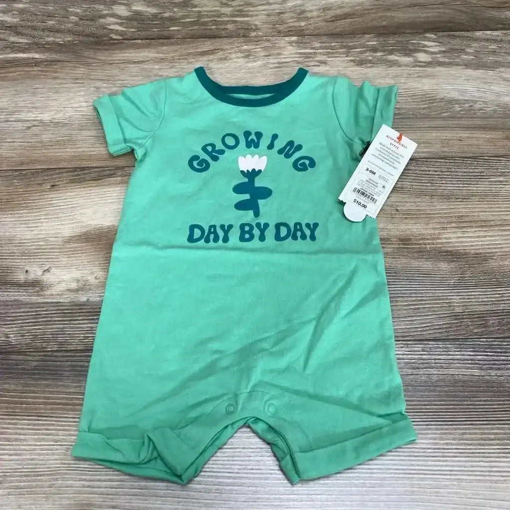 Front flat lay of green Cat & Jack baby romper (3–6M) showing 'GROWING DAY BY DAY' text and flower graphic, short sleeves and snap crotch on wood background
