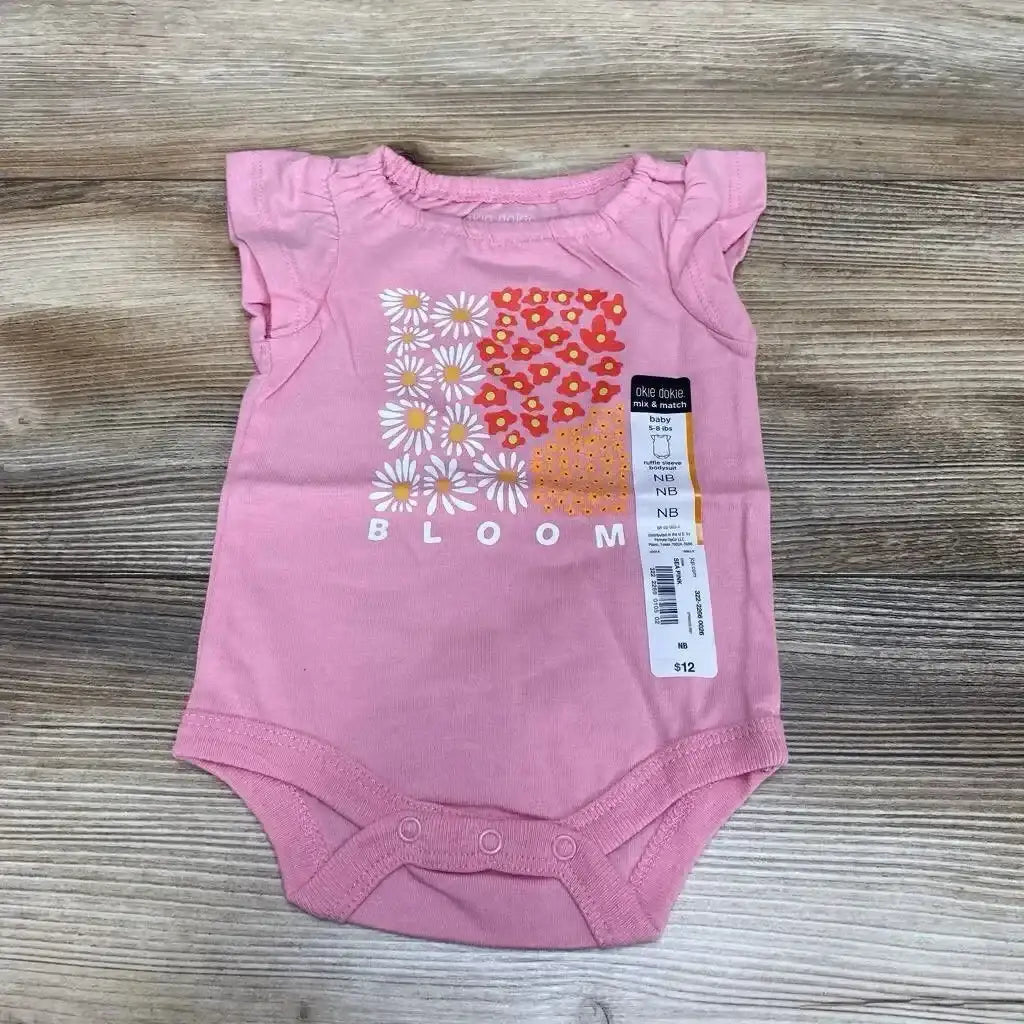 Front view of Okie Dokie bodysuit showcasing pink ruffle sleeve with Bloom daisy floral graphic and hangtag on wood plank floor