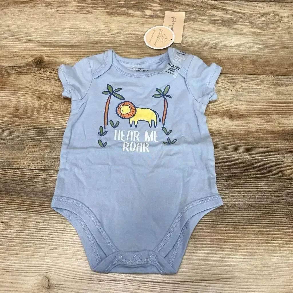Flat lay of blue baby bodysuit showcasing yellow lion graphic and 'HEAR ME ROAR' text on wood background