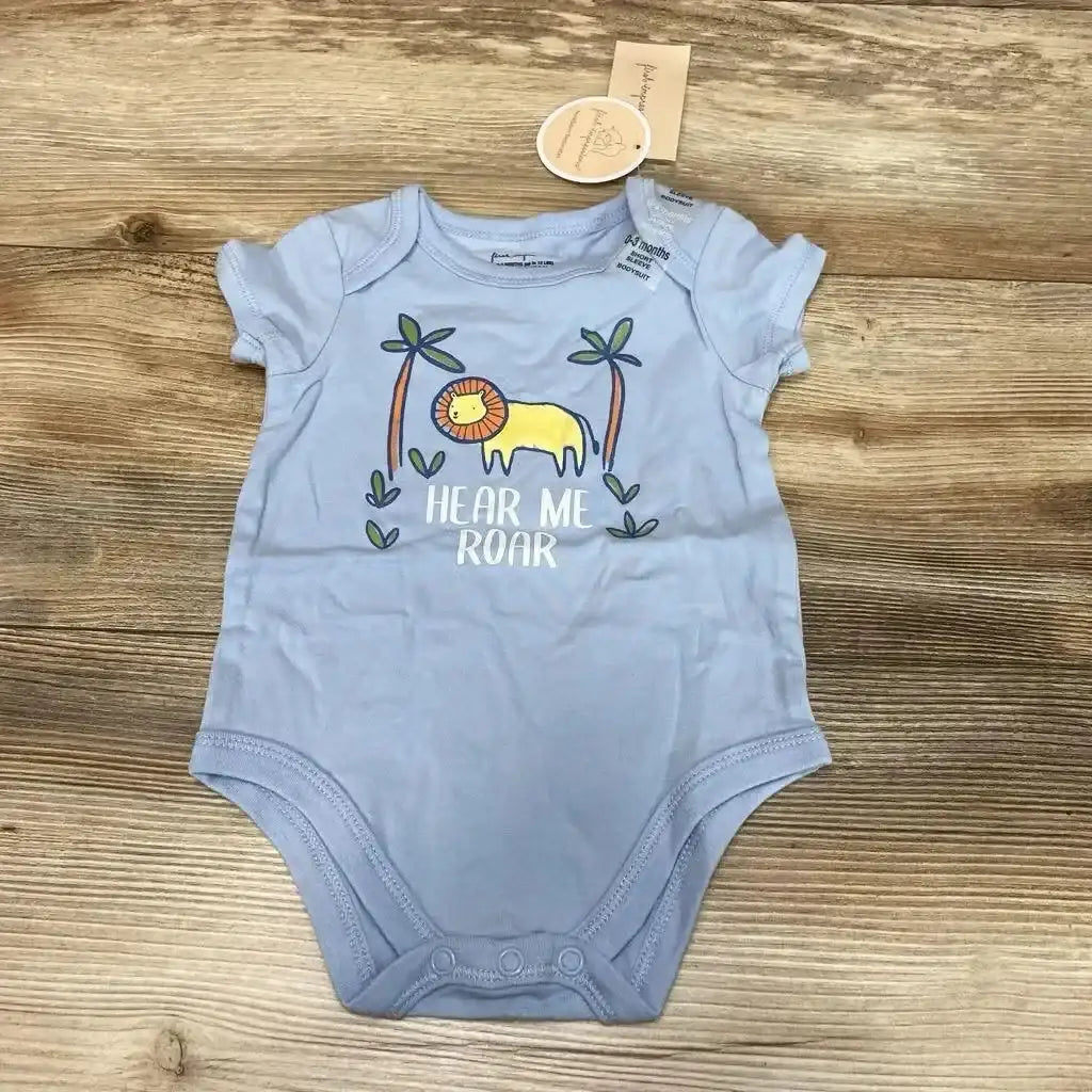 Flat lay of blue baby bodysuit showcasing yellow lion graphic and 'HEAR ME ROAR' text on wood background