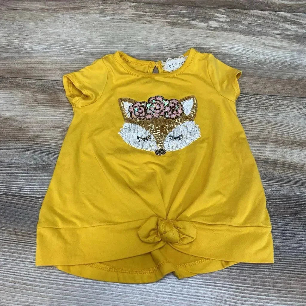 Flat lay of yellow short-sleeve toddler shirt showcasing sequin fox applique with floral crown and front knot on wood background