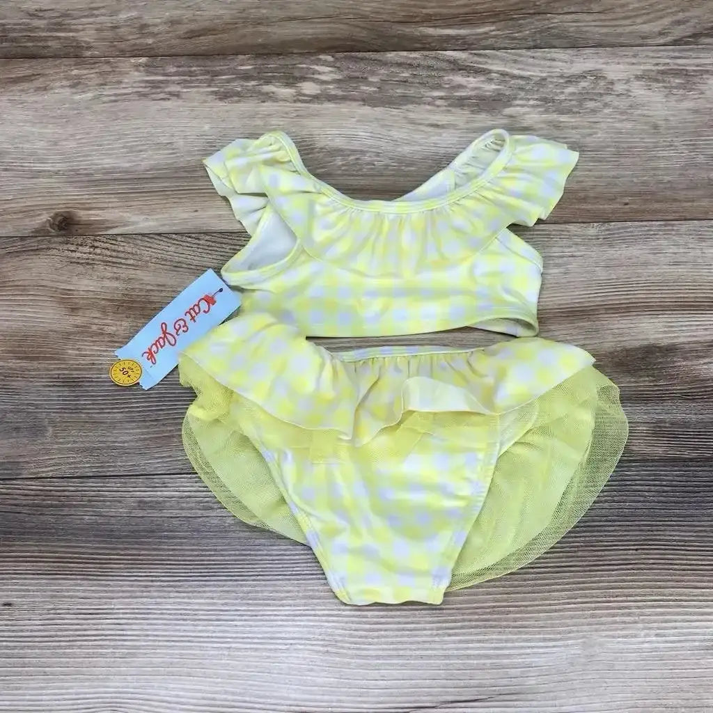 Flat lay of yellow gingham 2-piece toddler bikini with ruffled top and layered tulle skirted bottoms on wood background