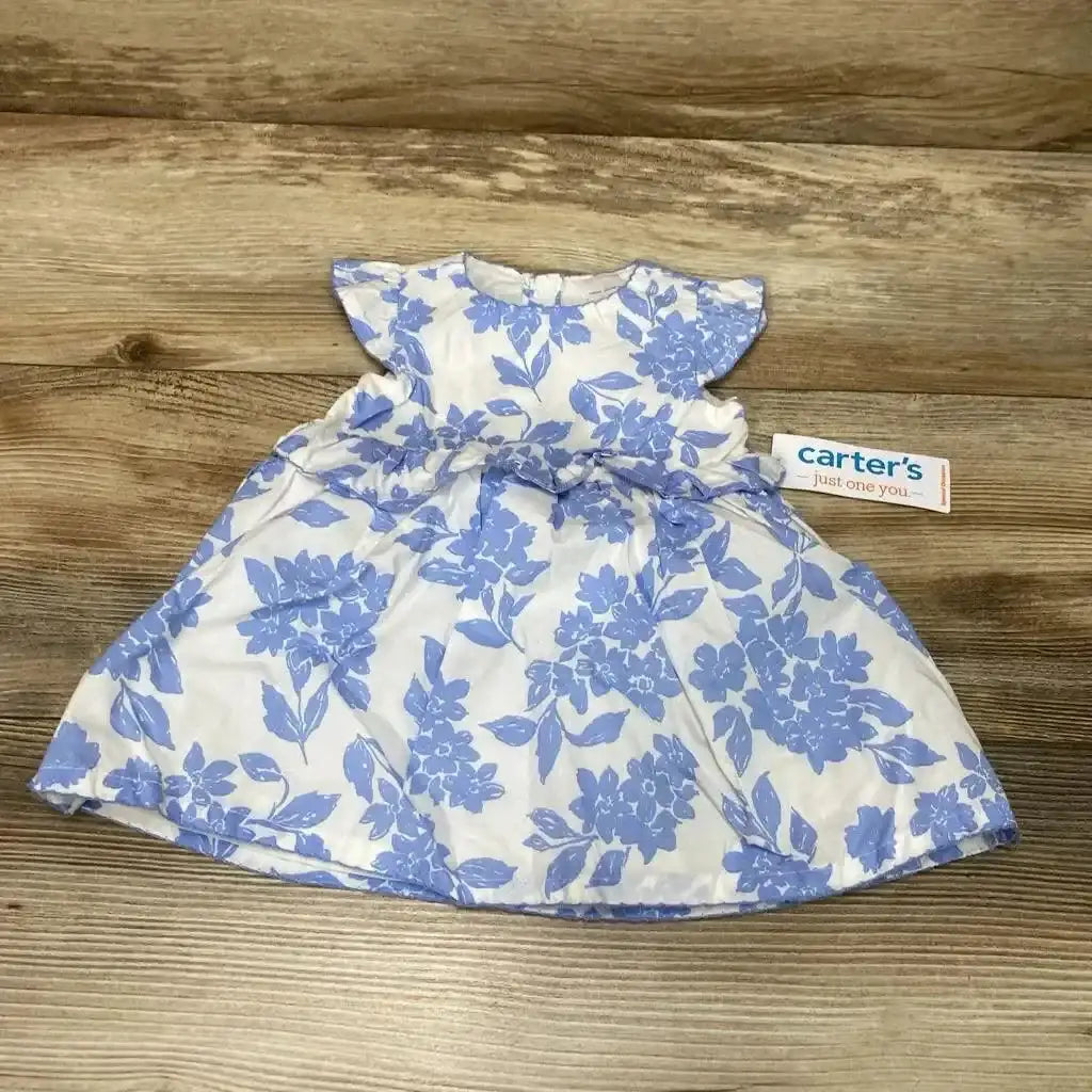 Flat lay of Just One You Carters white dress with blue floral print showcasing flutter sleeves bow waist and brand hangtag on wood plank floor