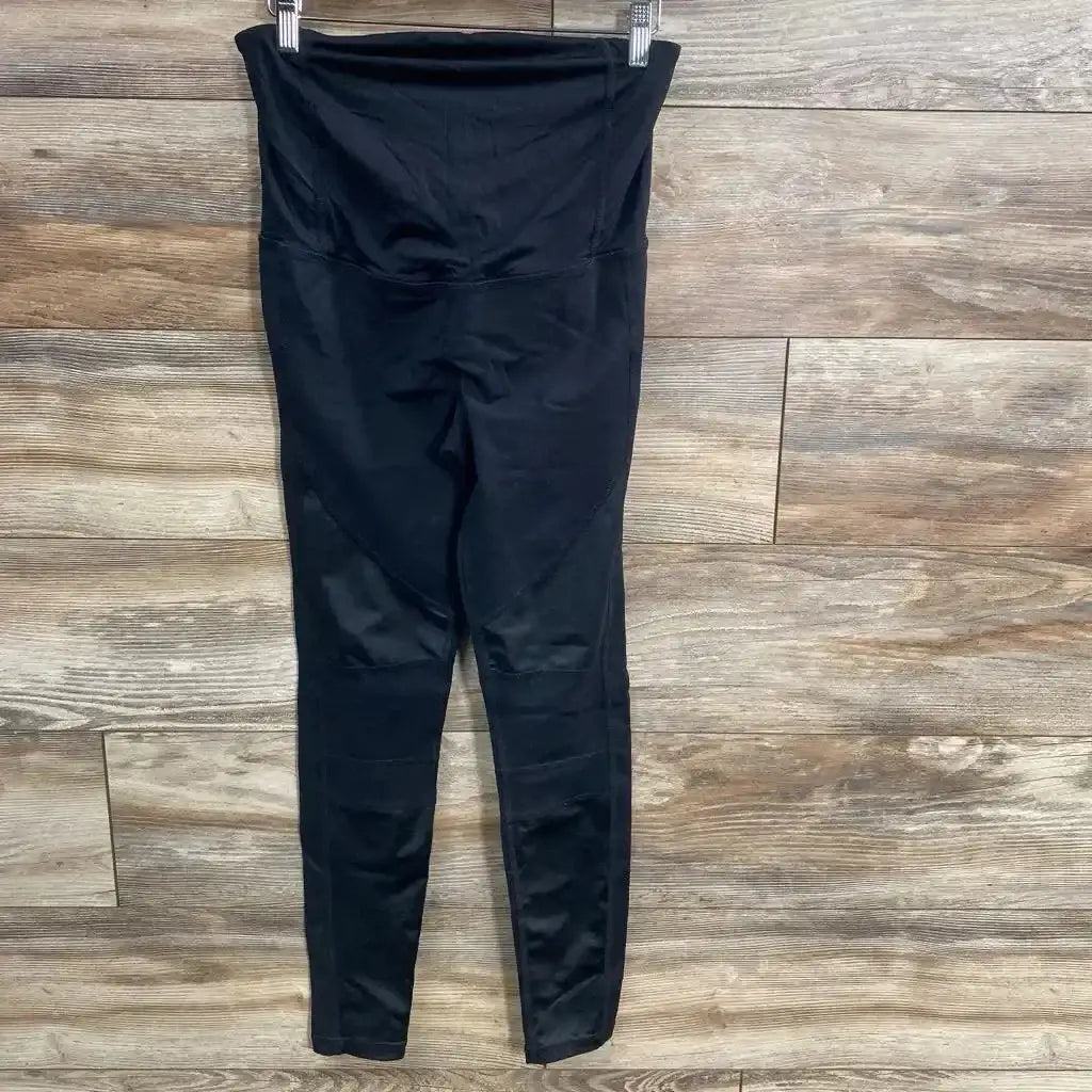 Flat lay of black maternity crossover-panel leggings showing high crossover waistband and full-length legs on wood floor