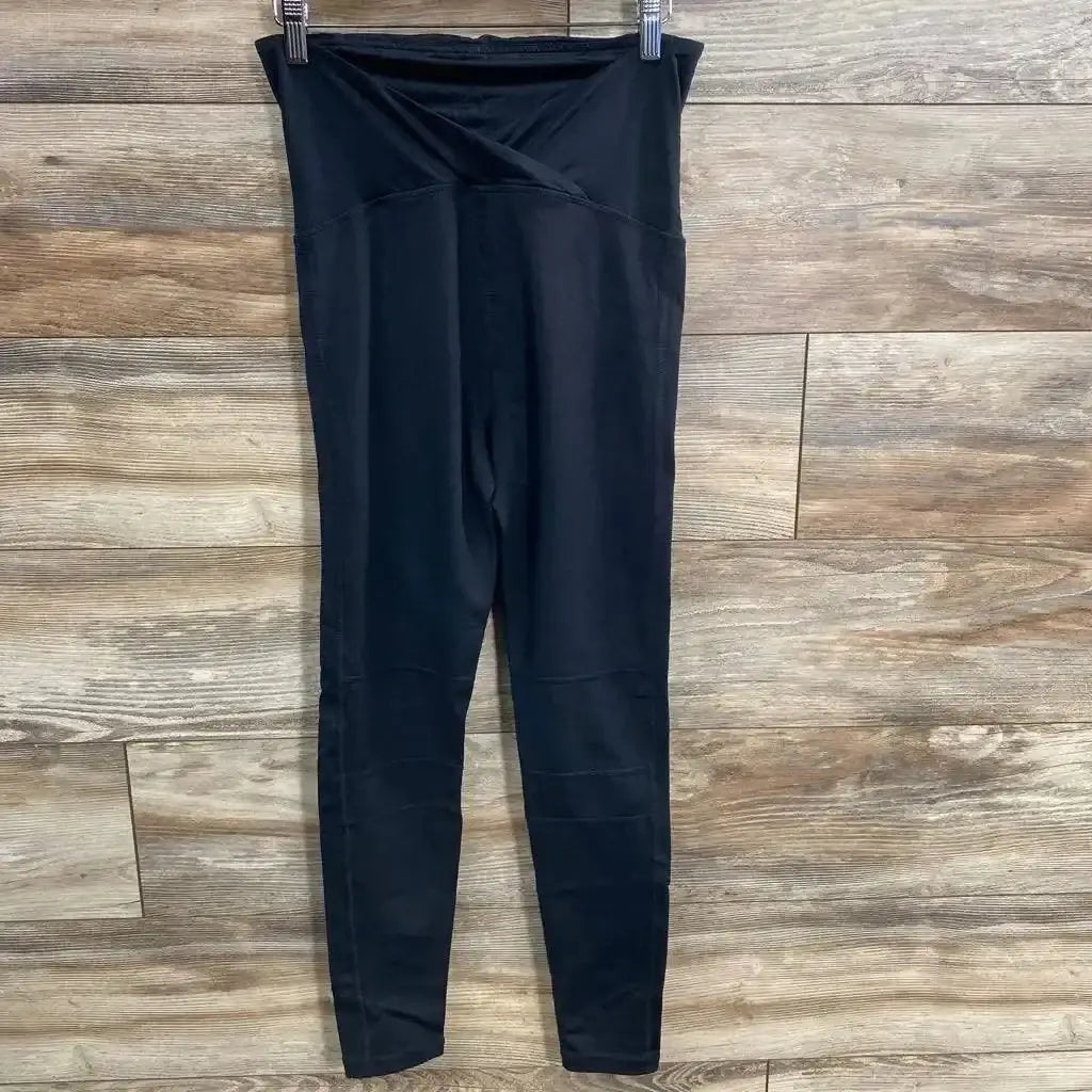 Front view of black Isabel maternity leggings with crossover belly panel and tapered legs on wood-plank background