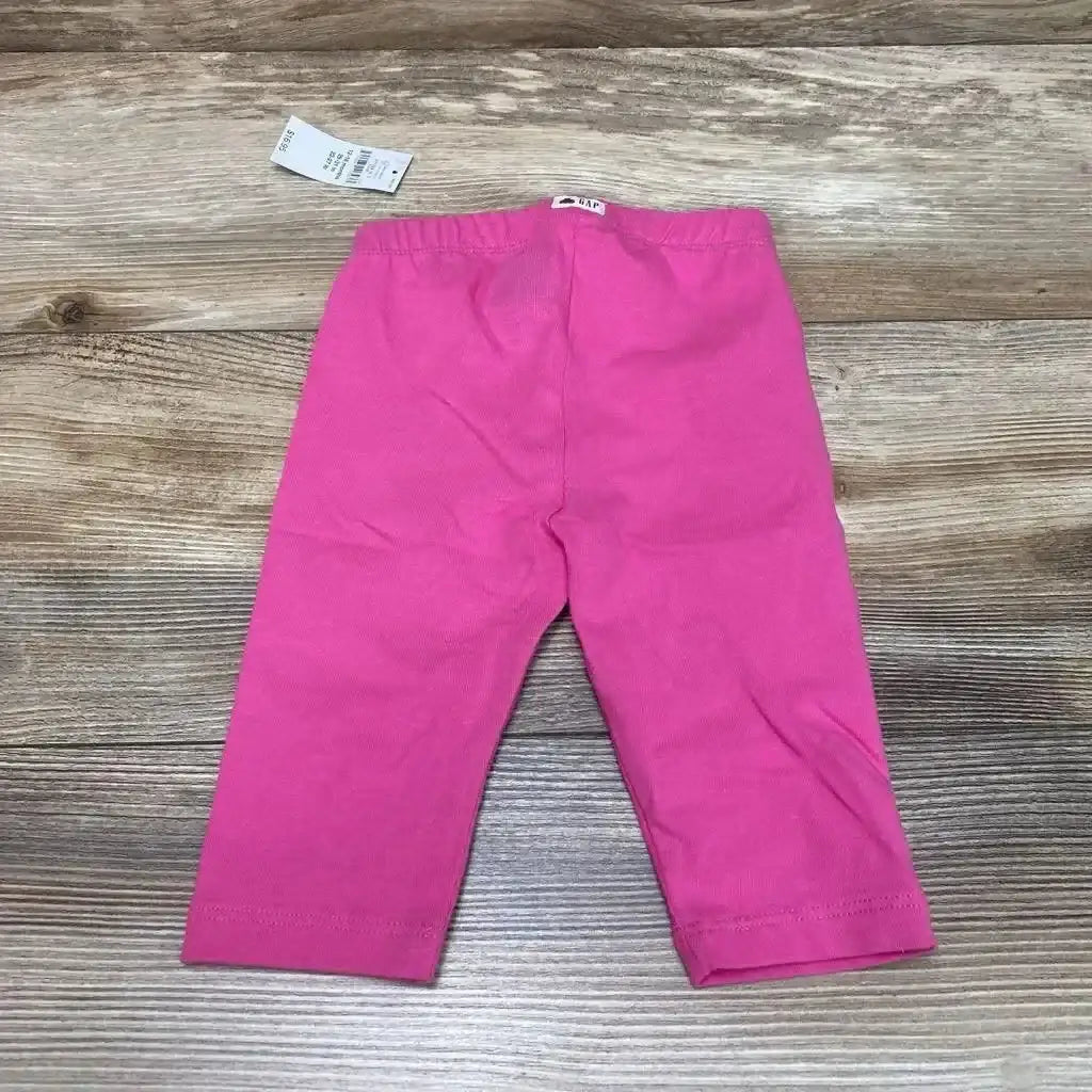 Back view of NWT BabyGap solid leggings in hot pink showcasing elastic waistband with Gap logo tag and brand hangtag on wood plank floor