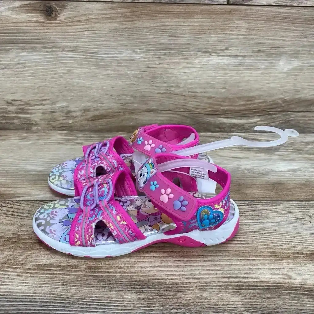 Side view of pink Paw Patrol ankle-strap sandals with Velcro straps and character paw-print details on wood background