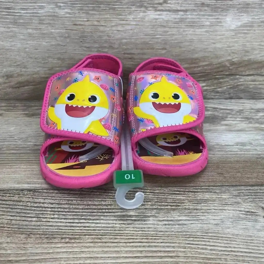 Front view of pink Baby Shark water sandals showing shark face on Velcro straps and size 10 hanger on wood background