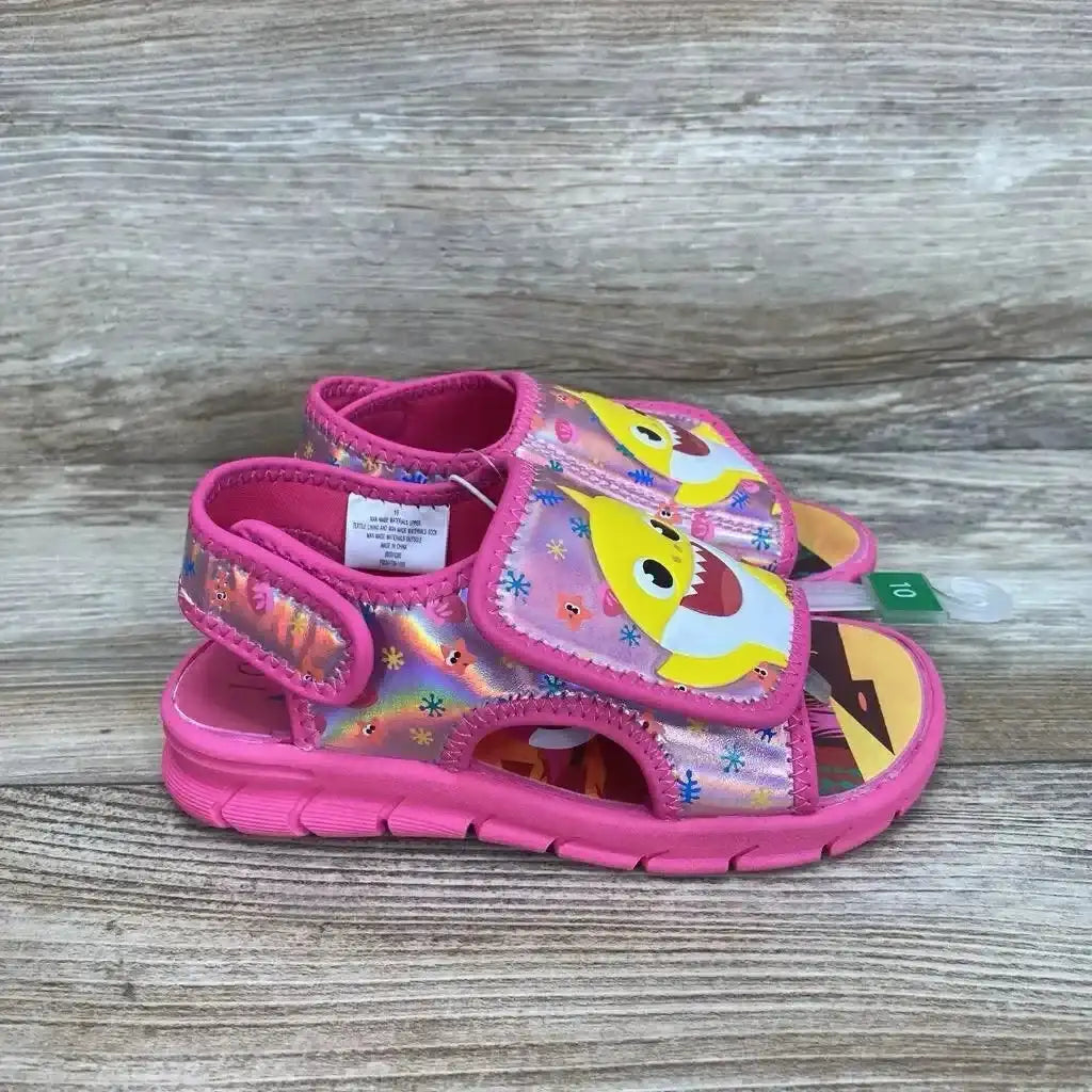 Side view of pink Pinkfong Baby Shark water sandals size 10C with shark-face graphic and velcro straps on wood background