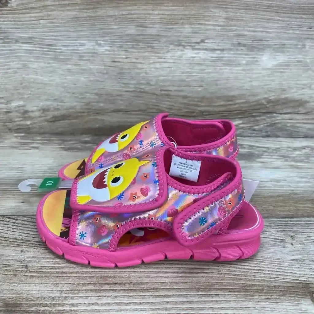 Side view of Pinkfong Baby Shark pink toddler water sandals size 10C with character print and Velcro straps on wood