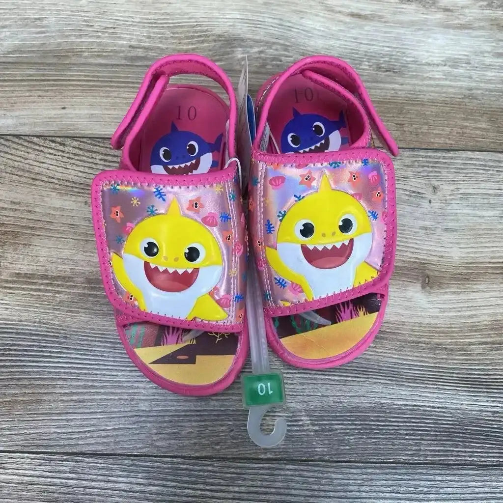 Top view of pink Baby Shark water sandals showcasing yellow Baby Shark on Velcro straps and size 10c hanger on wood floor