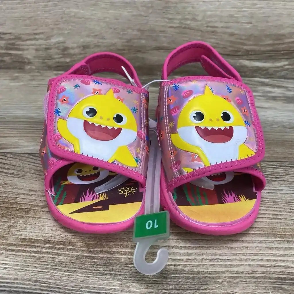 Front view of Pinkfong Baby Shark water sandals 10C with pink velcro character straps and illustrated insole on wood floor