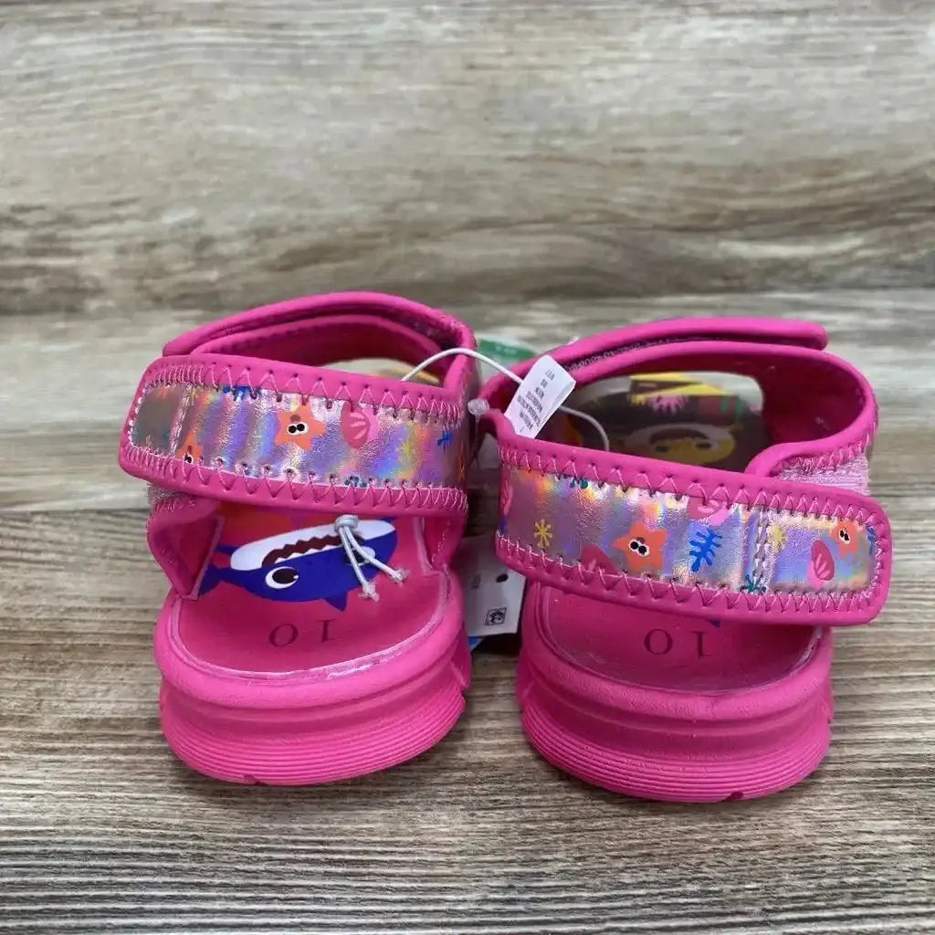 Back view of NEW Pinkfong Baby Shark Water Sandals size 10c showcasing pink sandals with iridescent shark print straps and hangtag on wood plank backdrop