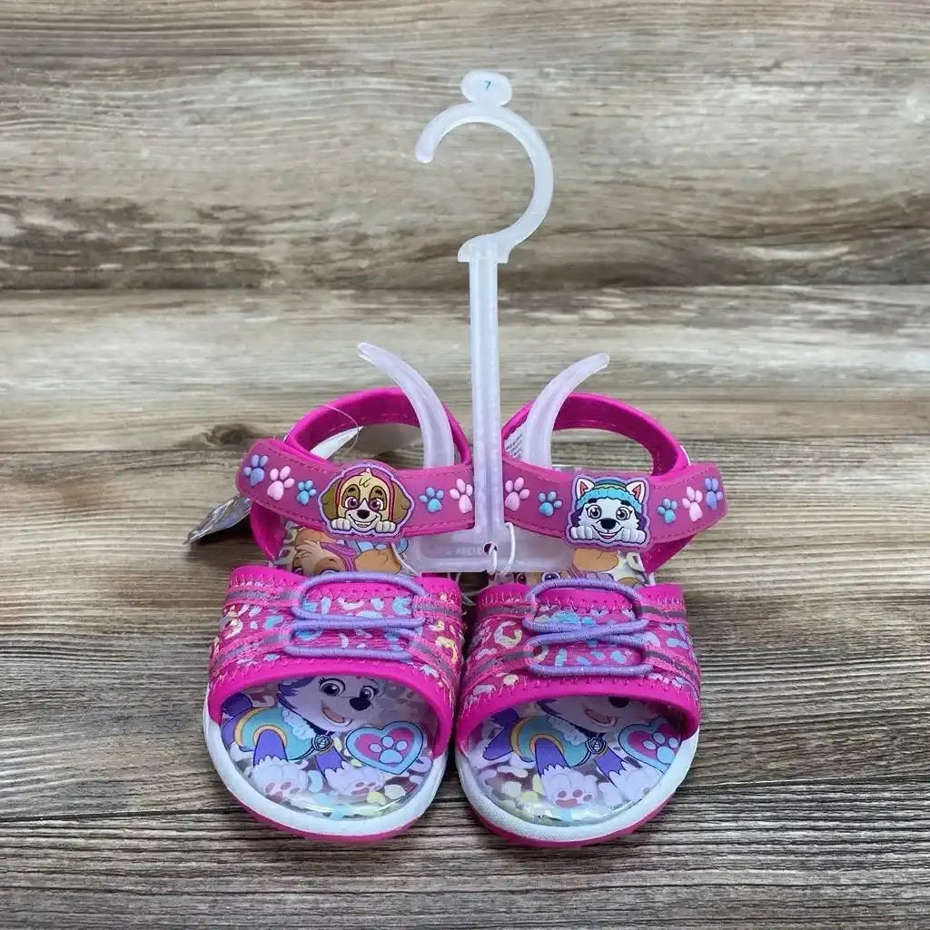 Front view of pink Paw Patrol toddler ankle-strap sandals size 7C showing character graphics on the footbed and Velcro straps on a wood background