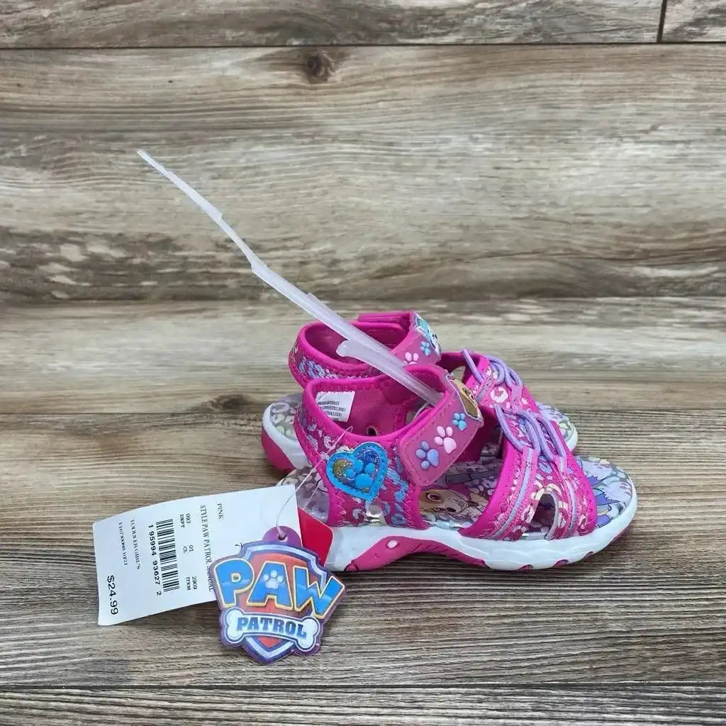 Side view of NWT Paw Patrol Adventure ankle strap sandals size 7c showcasing pink straps Skye charm and Paw Patrol hangtag on wood plank floor