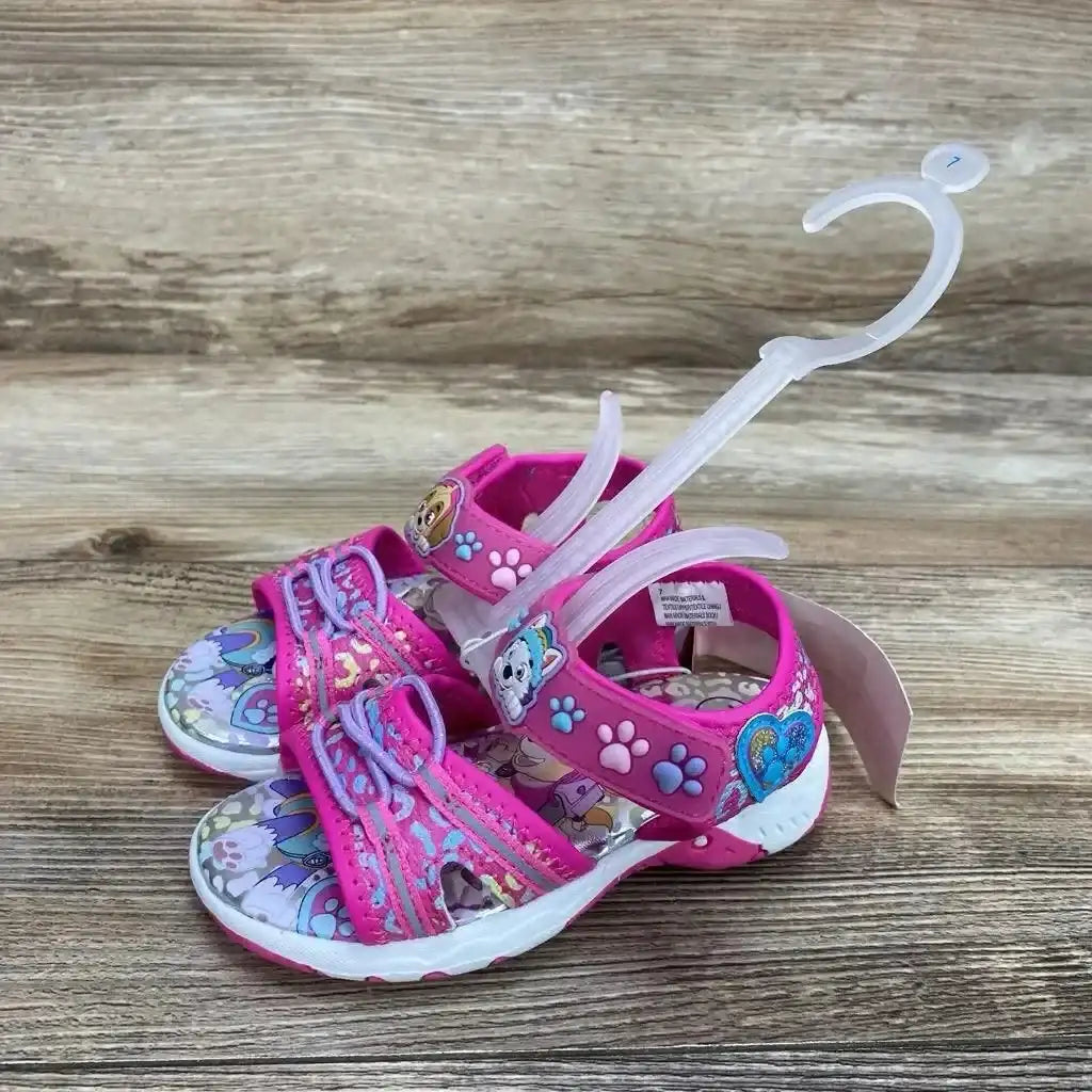 Three-quarter view of pink Paw Patrol sandals size 7C with adjustable ankle strap, character badge and paw accents on wood