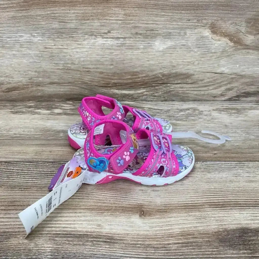 Side-angle pink Paw Patrol toddler sandals with Velcro ankle straps and paw-print heart accents on wood background