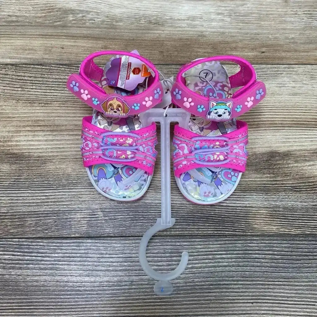 Top view of pink Paw Patrol ankle-strap toddler sandals size 7C with character patches, paw-print straps on wood background