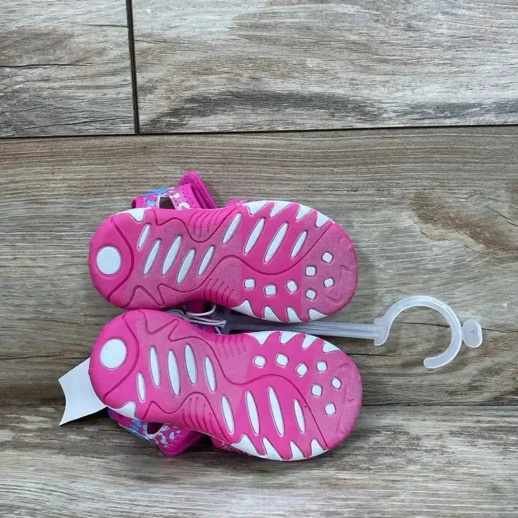 Bottom view of pink Paw Patrol toddler sandals, size 7C, showing pink and white textured soles on wood background