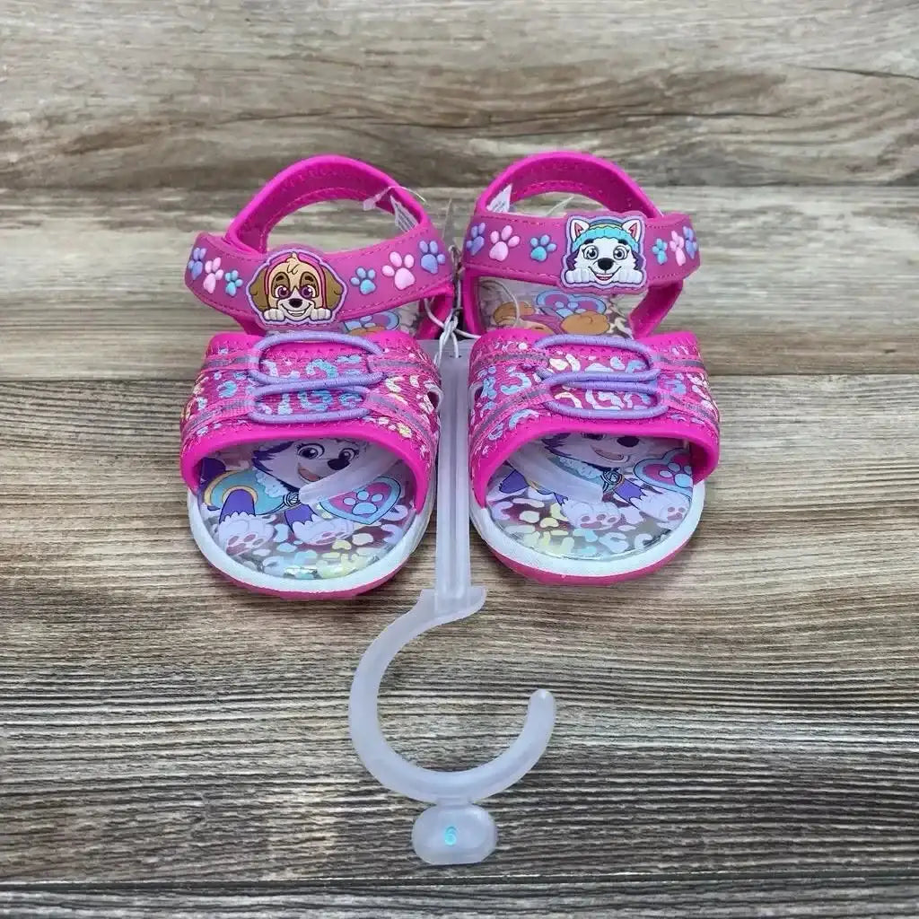 Front view of pink Paw Patrol ankle-strap sandals size 9C showing character patches and adjustable Velcro straps on wood