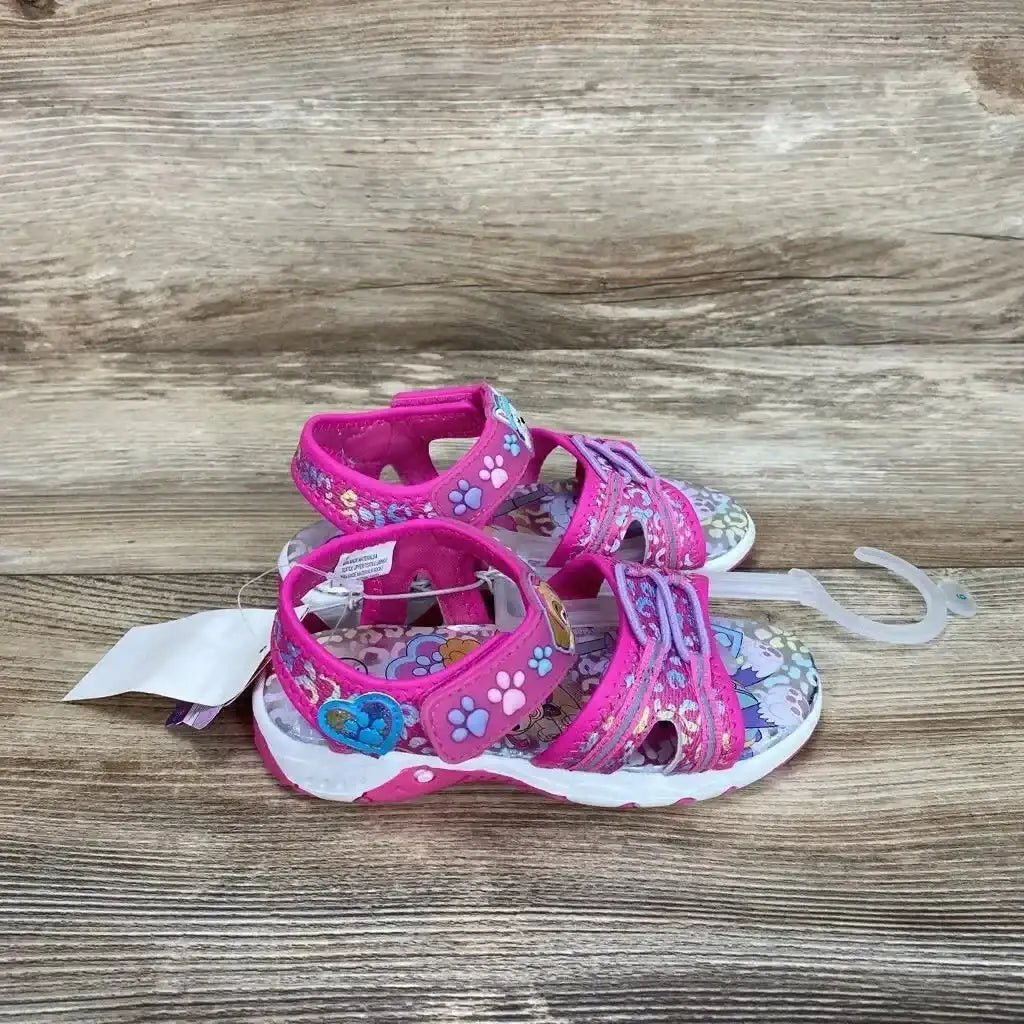 Side view of pink Paw Patrol ankle-strap sandals size 9C showing paw-print straps, heart patch, floral insole on wood