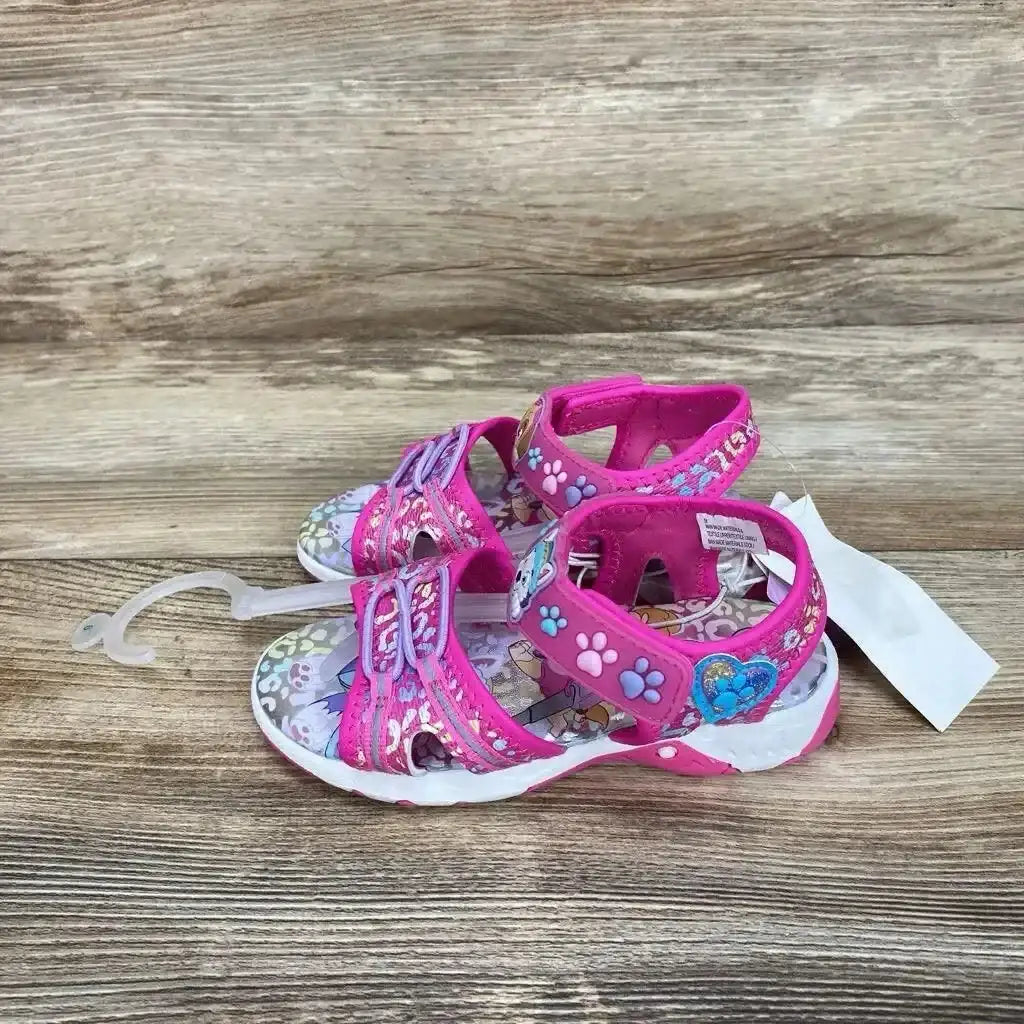 Side view of pink Paw Patrol ankle-strap sandals size 9C showcasing paw-print and heart decorations on wooden floor background