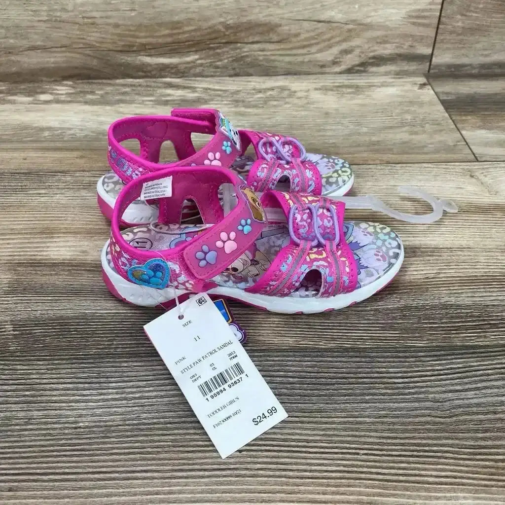 Side view of pink Paw Patrol ankle-strap sandals size 11C showing paw-print straps and character insole on wood surface