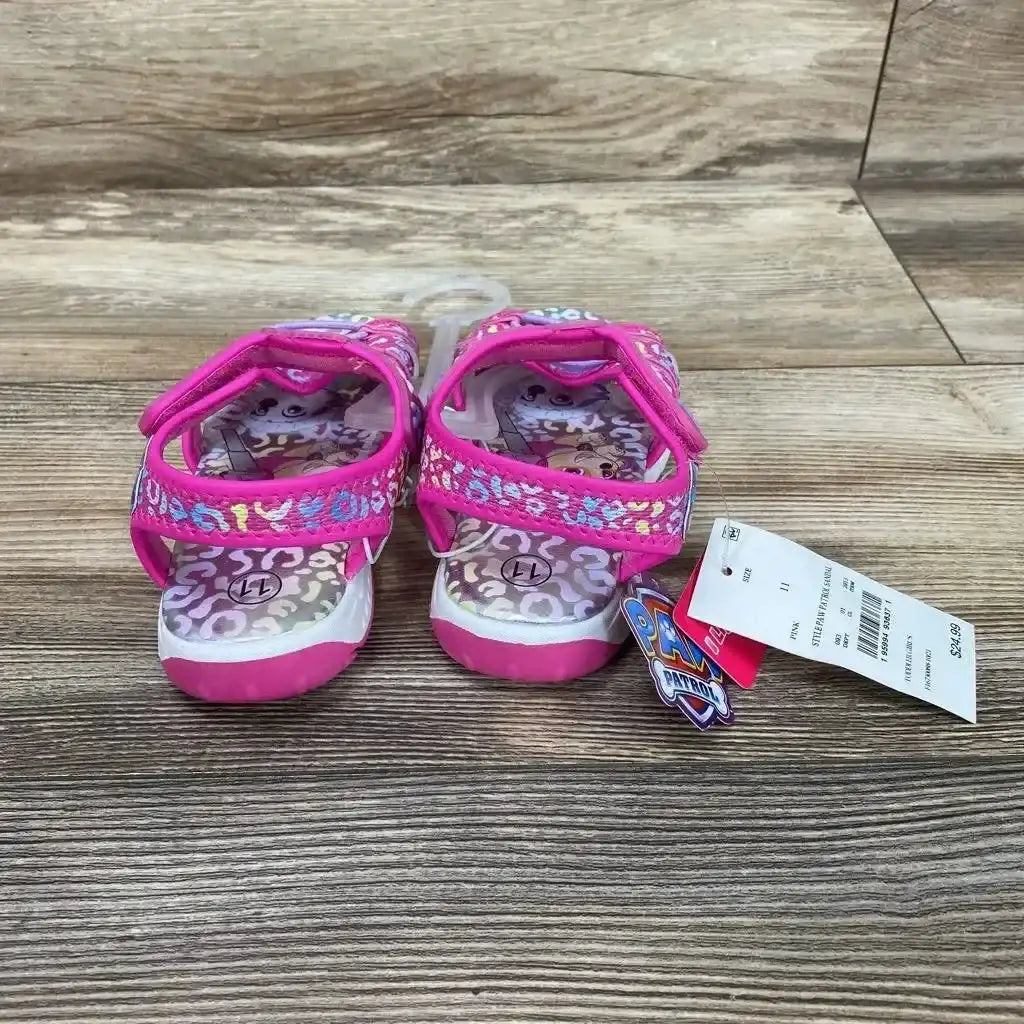Front view of pink Paw Patrol ankle-strap toddler sandals showing velcro straps, character insoles, and size tag on wood floor