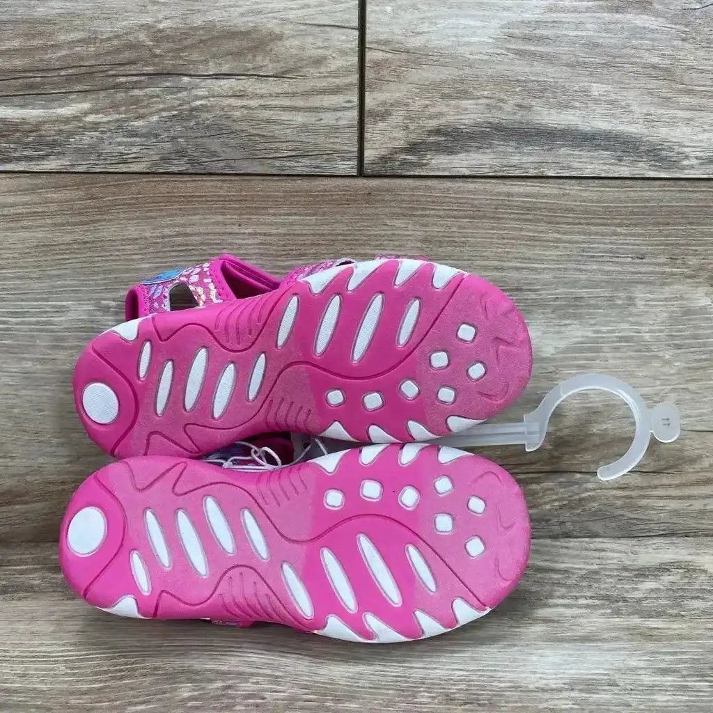 Bottom view of pink Paw Patrol ankle strap sandals showing pink and white tread pattern and size hanger on wood floor