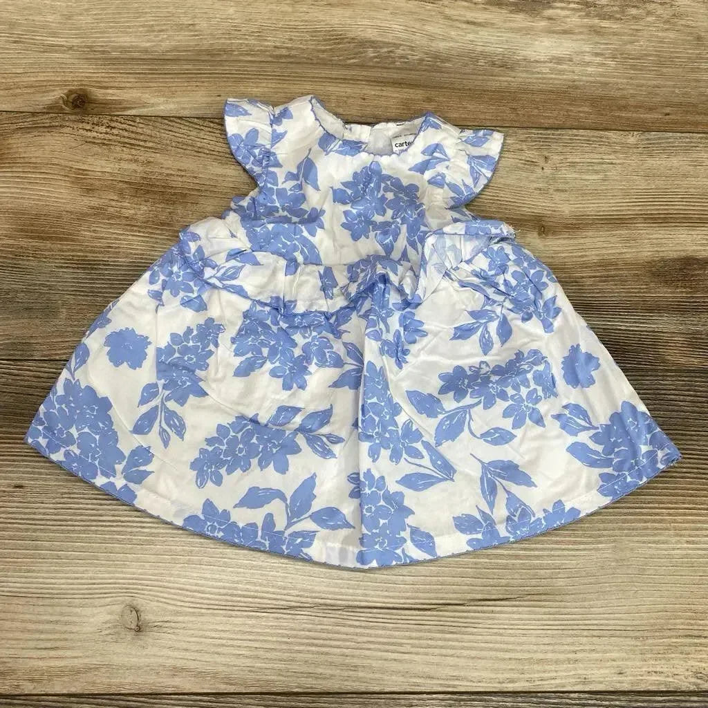 Flat lay of newborn white dress with blue floral print and matching bloomers showcasing flutter sleeves and gathered skirt on wood background